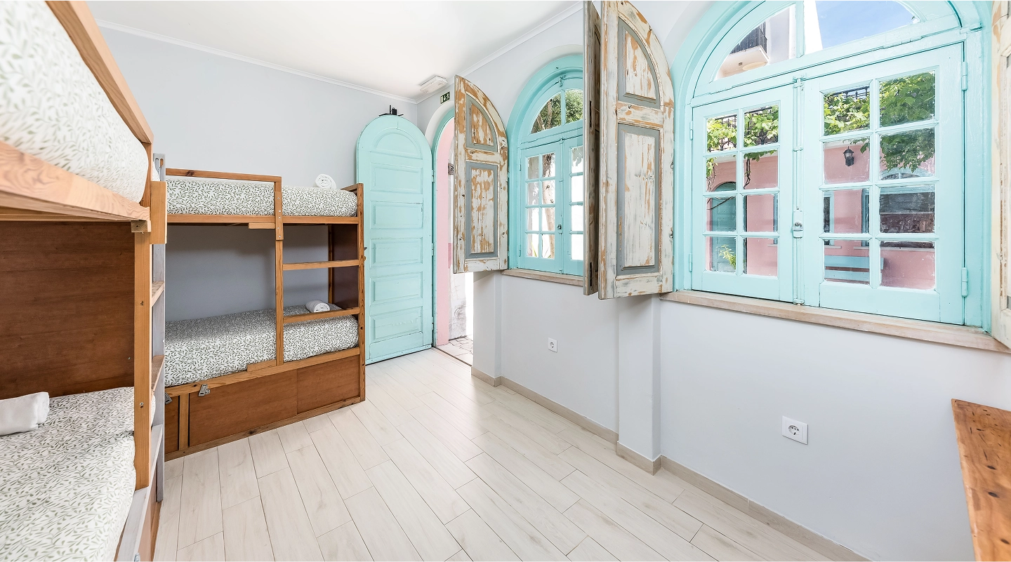 Bright room with wooden bunk beds, light blue arched windows with rustic shutters, and a matching blue door.