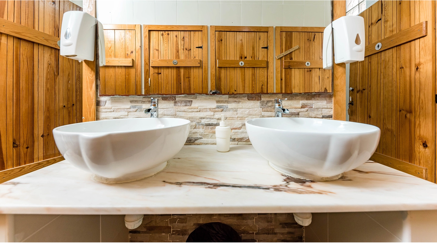 Double white sink countertop with wooden panel walls and rustic wooden doors reflected in mirrors.