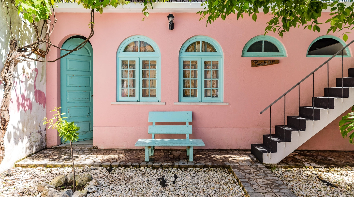 Pink house exterior with turquoise door, arched windows, bench, and outdoor staircase labeled rooftop.